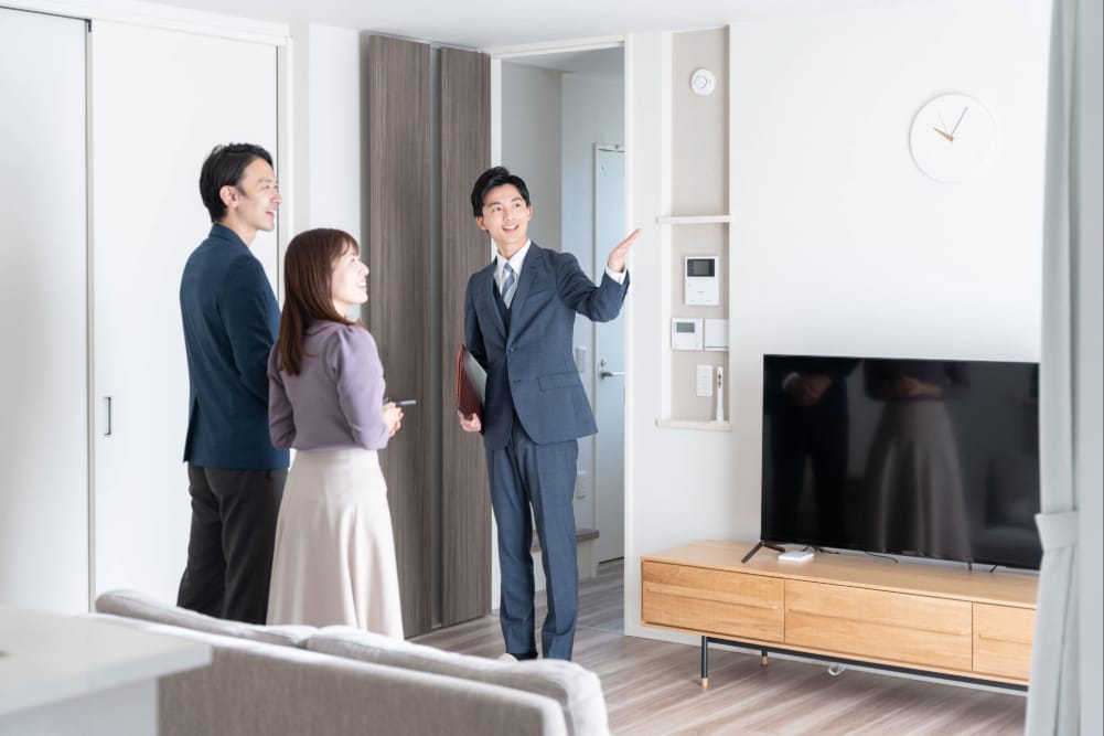 明るくモダンなリビングルームで、不動産エージェントがカップルに物件を案内している様子