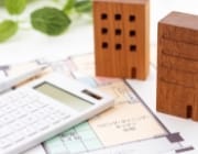 木製の建築模型、電卓、建築図面が配置された不動産計画のイメージ