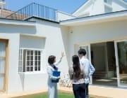 不動産エージェントが白いモダンな家の庭でカップルに物件を案内している様子