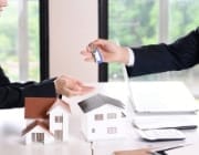 家型のキーホルダーが付いた鍵の束を差し出す人物。不動産の引き渡しを示す