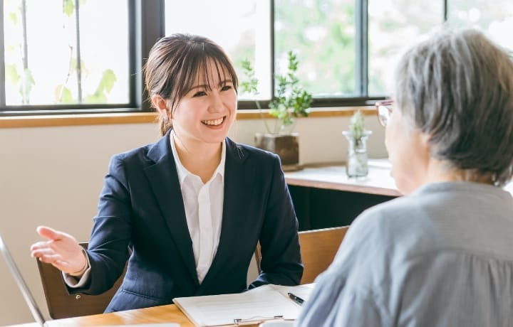 笑顔で顧客に説明するビジネスウーマン。書類を前に、年配の顧客と対話している様子