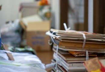 白い紐で束ねられた古い紙や本が積み重ねられた散らかった室内の様子