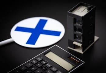電卓と建物模型、プラス記号のサインが配置された不動産関連のイメージ