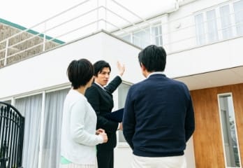 不動産エージェントがカップルに白いモダンな家を案内している様子