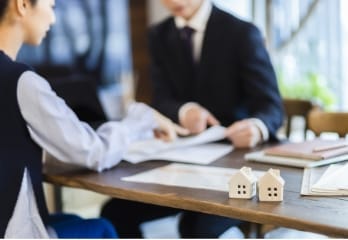 木製のテーブルを囲んで書類と住宅模型を検討する2人のビジネスパーソン